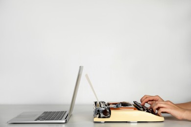 Woman using old typewriter near laptop at table against light background, closeup with space for text. Concept of technology progress