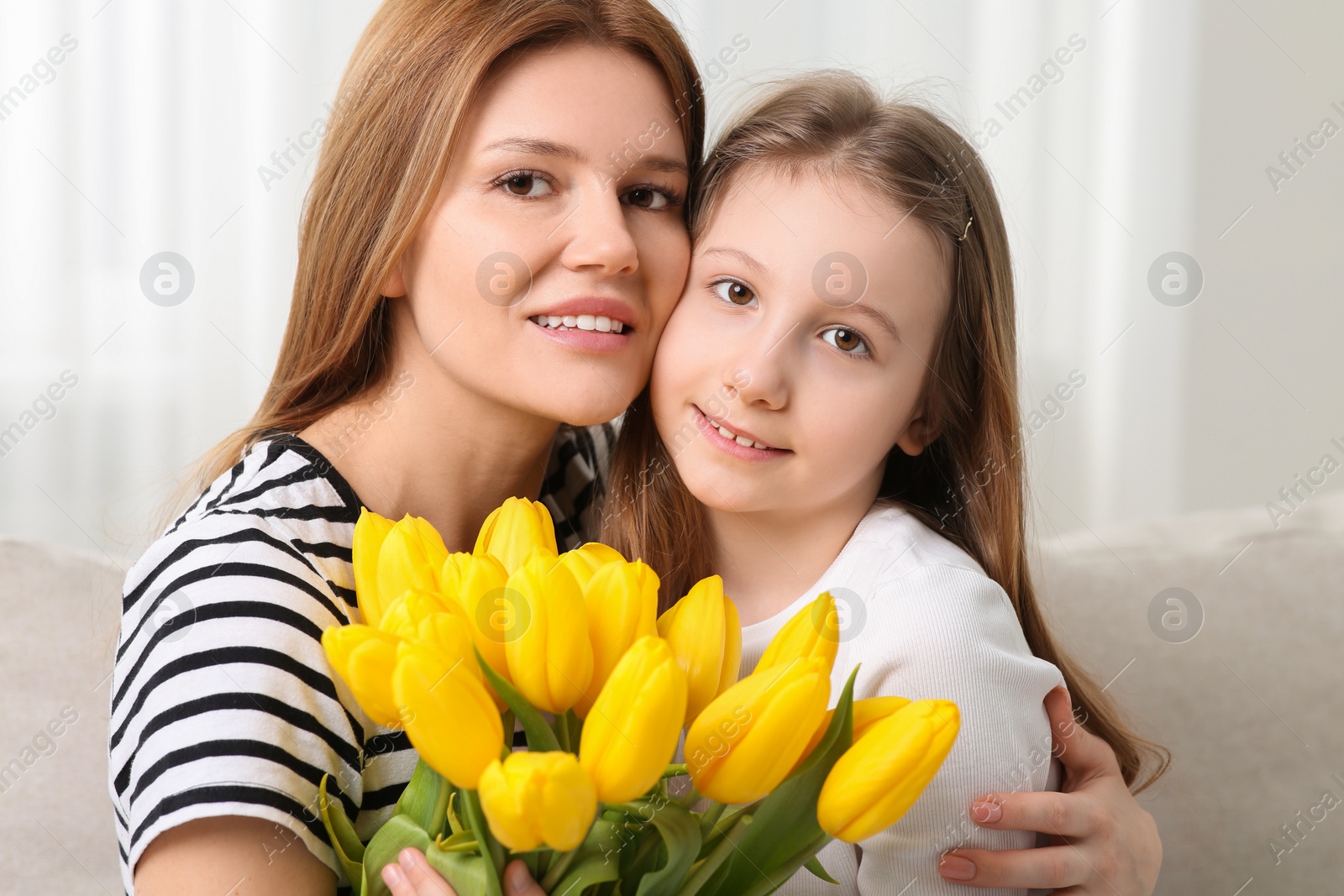 Photo of Happy mother and her cute daughter with bouquet of yellow tulips at home