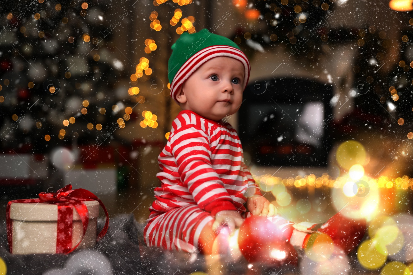 Image of Cute little baby wearing Santa's elf clothes with Christmas gift on floor at home