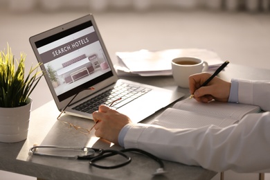 Doctor searching hotel using laptop at table, closeup. Booking online service