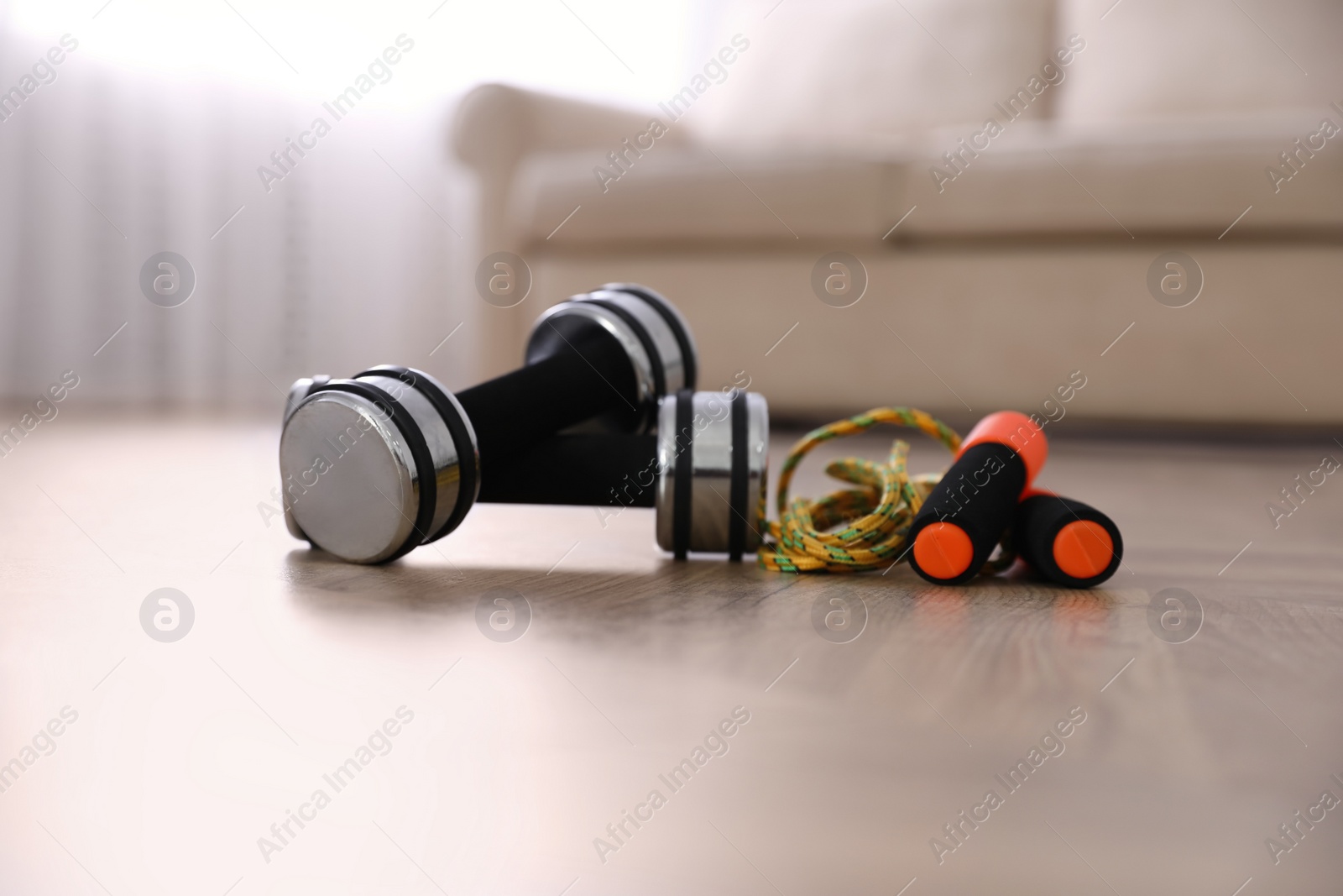 Photo of Dumbbells and jumping rope on floor in room. Home fitness