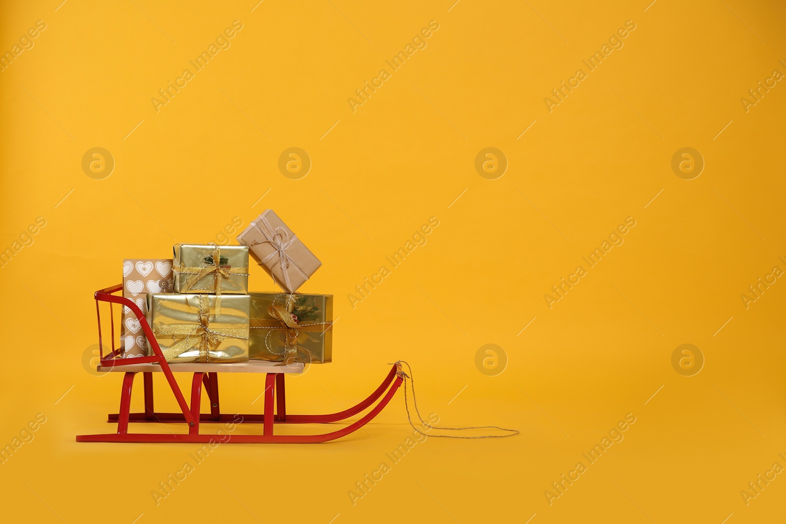 Photo of Sleigh with gift boxes on yellow background. Space for text