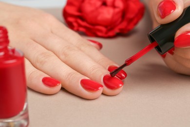 Photo of Woman painting nails with red polish on beige background, closeup