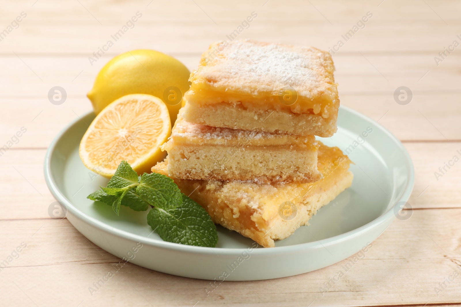 Photo of Tasty lemon bars with powdered sugar and mint on wooden table, closeup