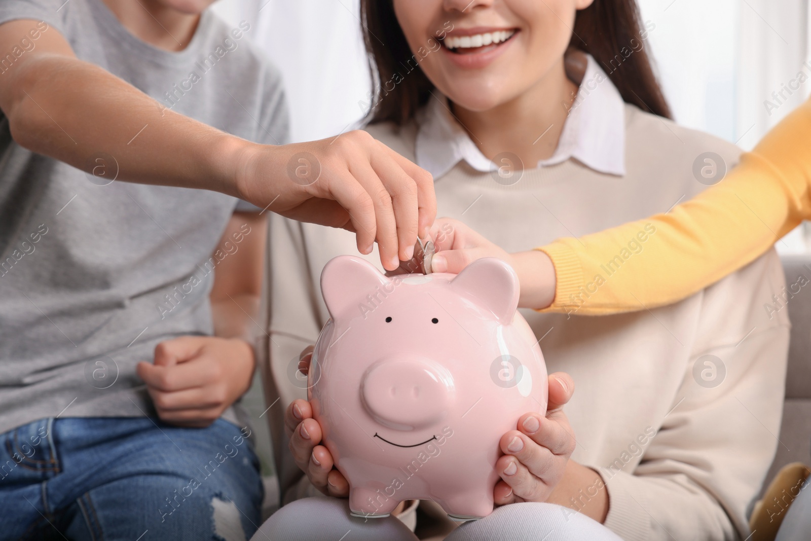 Photo of Happy family putting coins into piggy bank at home, closeup