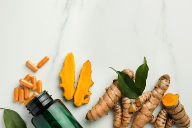 Photo of Turmeric roots, pills and bottle on white marble table, flat lay. Space for text