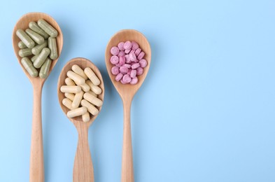 Different vitamin pills in wooden spoons on light blue background, flat lay. Space for text