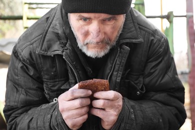 Poor homeless man holding piece of bread outdoors