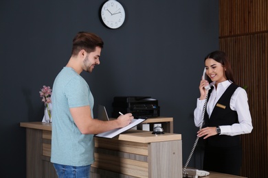 Client registering at desk while receptionist talking on phone in lobby