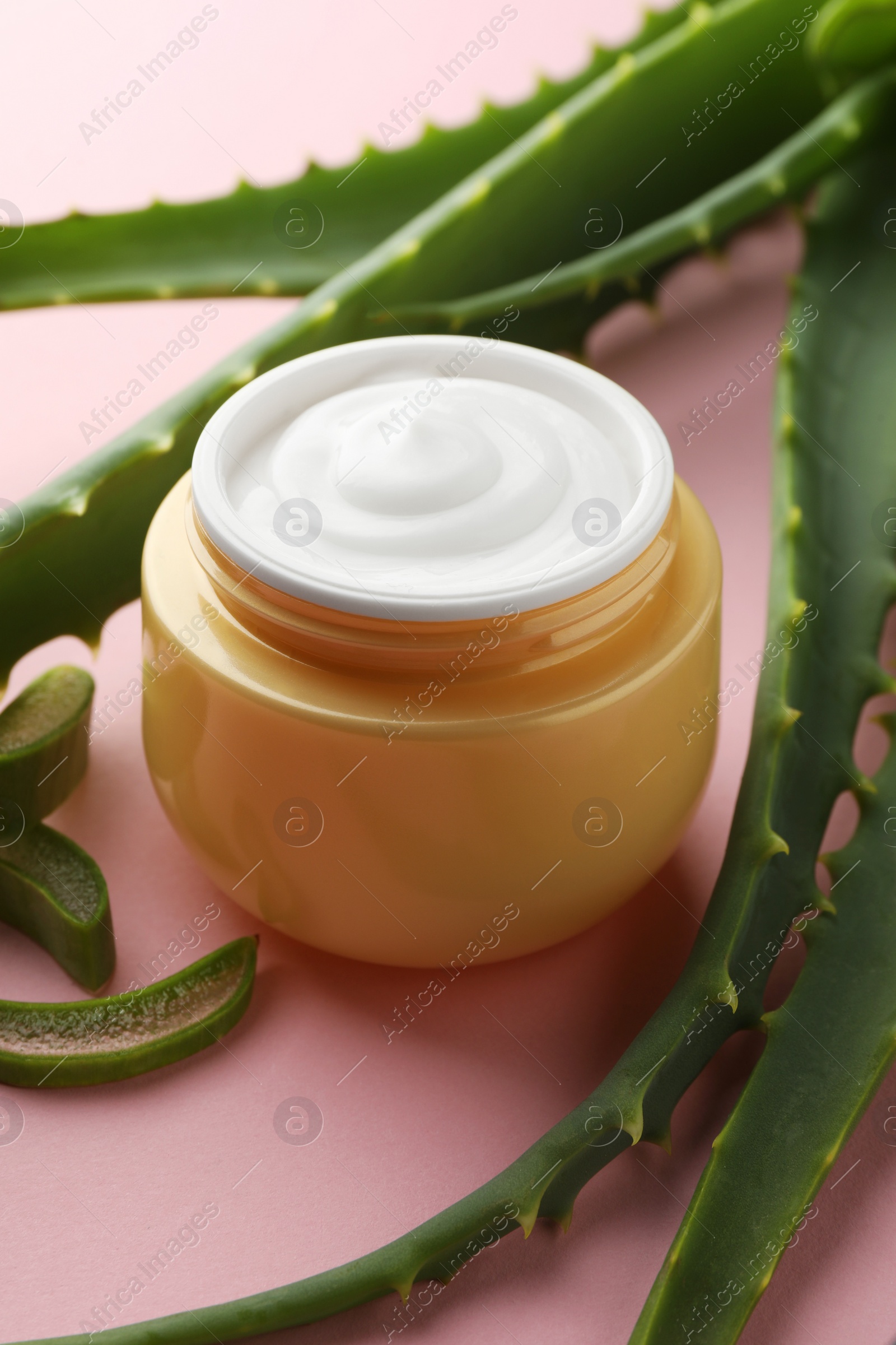 Photo of Jar with cream and cut aloe leaves on pink background, closeup