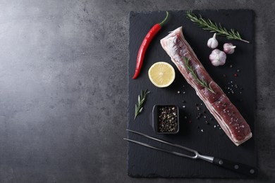 Piece of raw pork belly, rosemary, garlic, lemon and spices on grey textured table, top view. Space for text