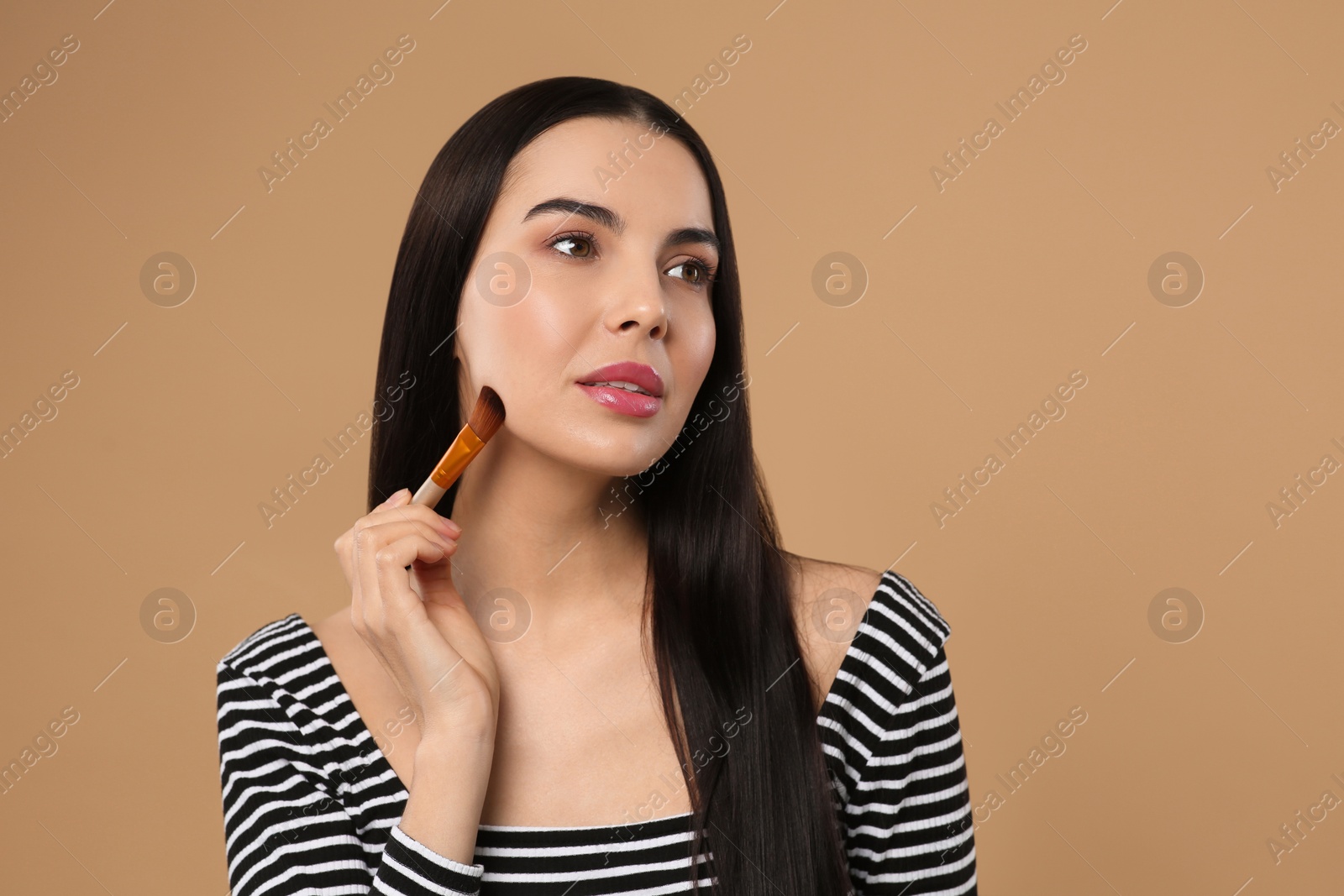 Photo of Beautiful woman applying makeup on light brown background. Space for text