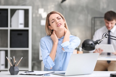 Photo of Young woman suffering from neck pain in office