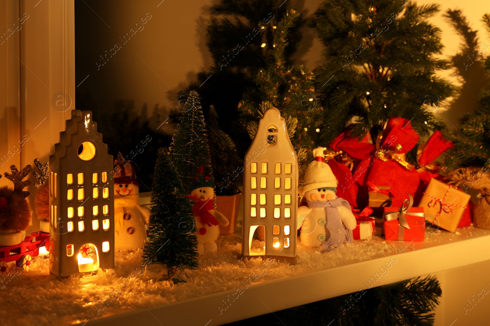 Photo of Christmas atmosphere. Beautiful glowing houses, fir trees and toys on window sill indoors