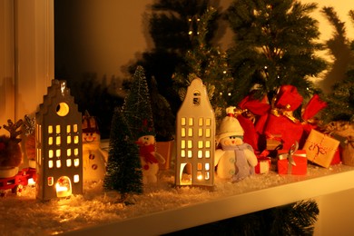 Christmas atmosphere. Beautiful glowing houses, fir trees and toys on window sill indoors