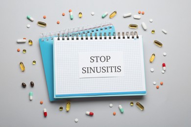 Photo of Notebook with word SINUSITIS surrounded by different pills on grey background, flat lay
