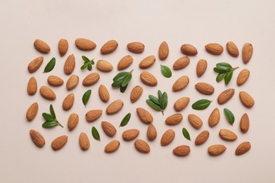 Photo of Delicious almonds and fresh leaves on beige background, flat lay