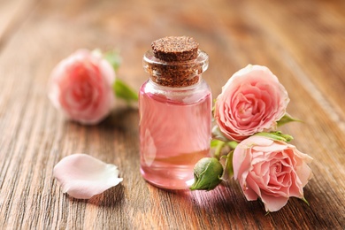 Photo of Bottle of rose essential oil and flowers on wooden table