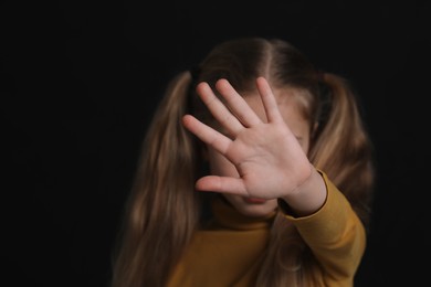 Photo of Girl making stop gesture against black background, focus on hand and space for text. Children's bullying