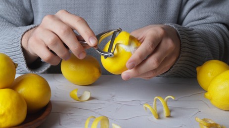 Photo of Man peeling lemon at white textured table, closeup