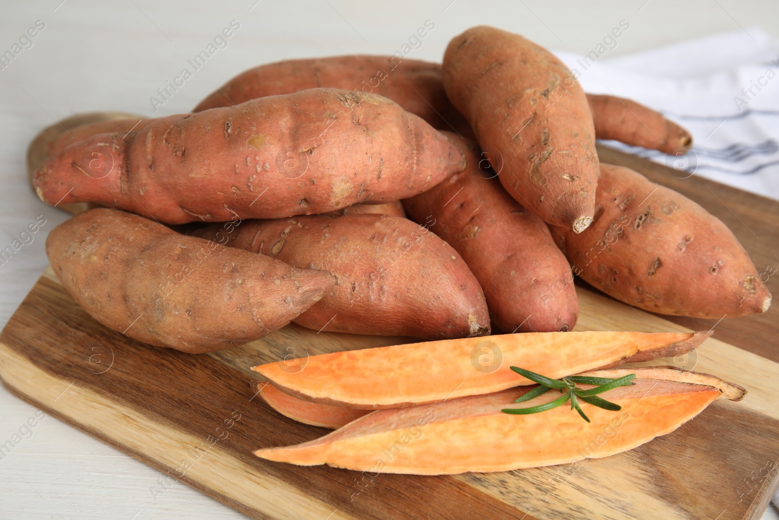 Photo of Wooden board with cut and whole sweet potatoes on white table, closeup