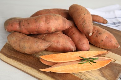 Photo of Wooden board with cut and whole sweet potatoes on white table, closeup
