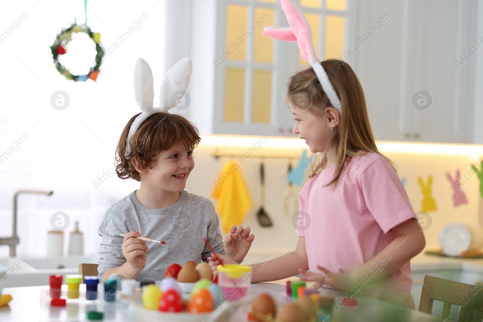 Photo of Easter celebration. Cute children with bunny ears painting eggs at table in kitchen