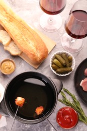 Fondue pot, forks with fried meat pieces, glasses of red wine and other products on grey textured table, flat lay