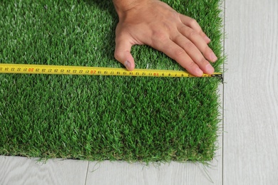 Photo of Man measuring artificial grass carpet indoors, above view