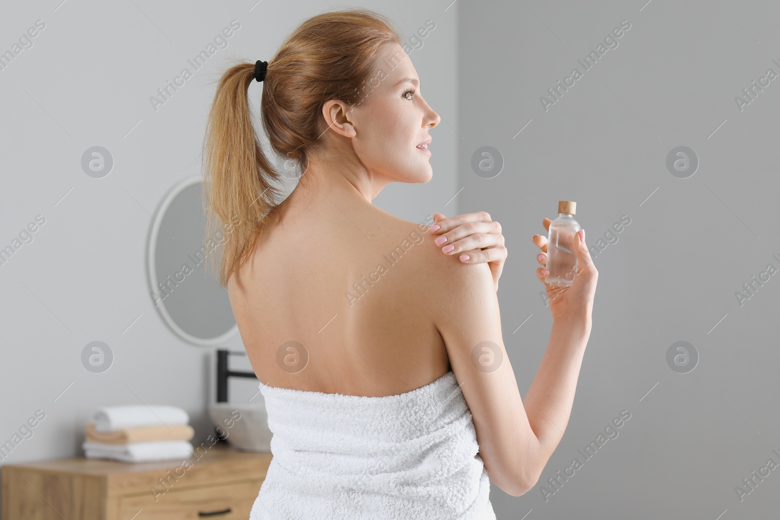 Photo of Beautiful woman applying body oil onto shoulder in bathroom