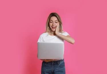 Young woman with modern laptop on pink background