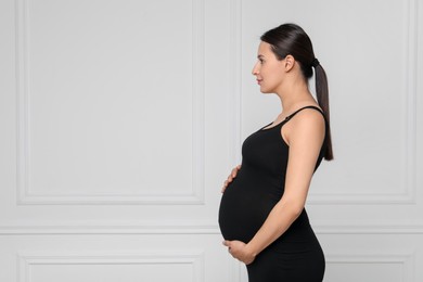 Beautiful pregnant woman in black dress near light grey wall, space for text