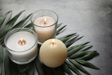 Burning wax candles and tropic leaf on table