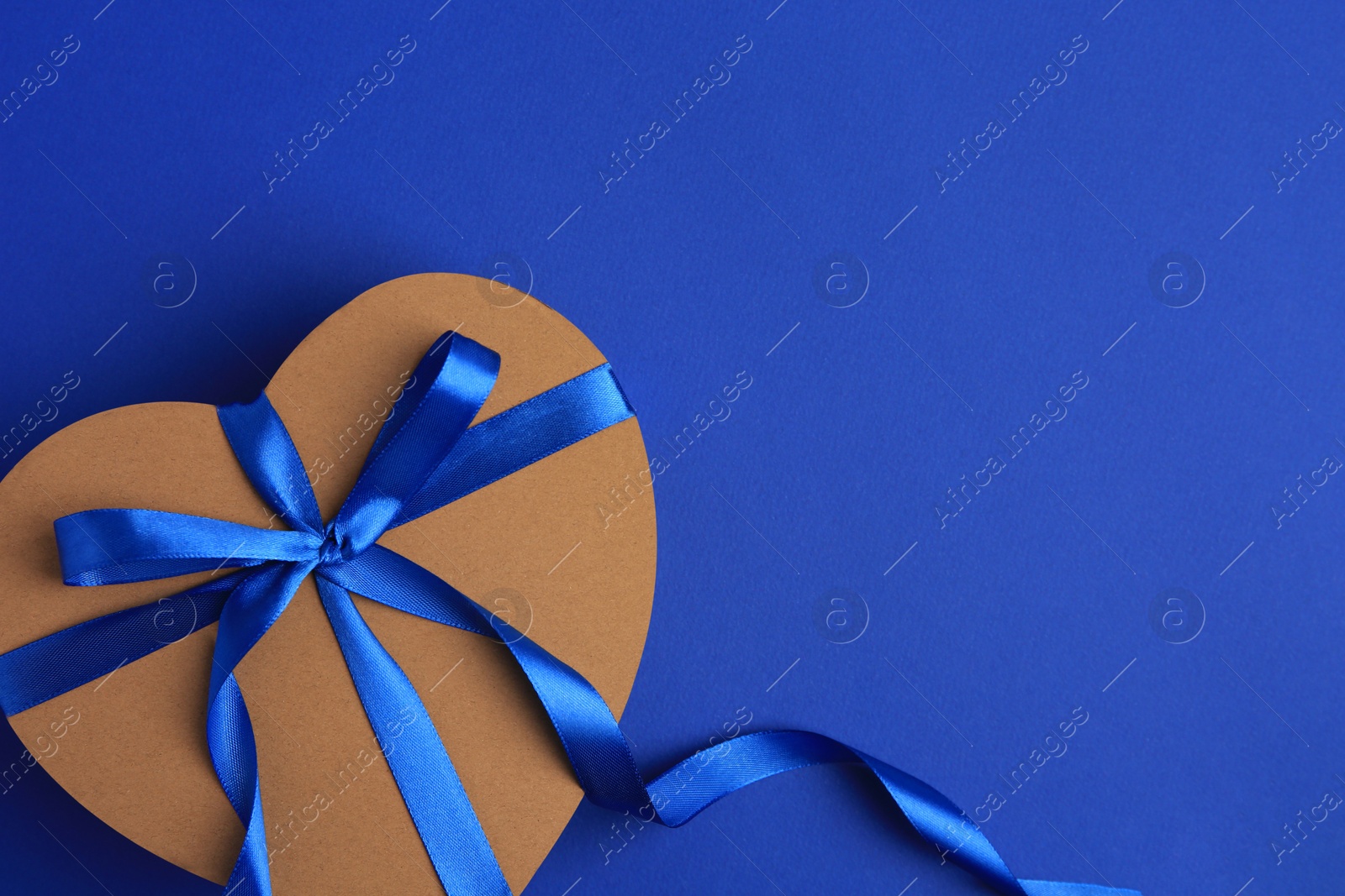 Photo of Beautiful heart shaped gift box with bow on blue background, top view. Space for text