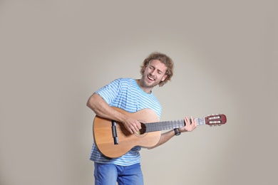 Young man playing acoustic guitar on grey background