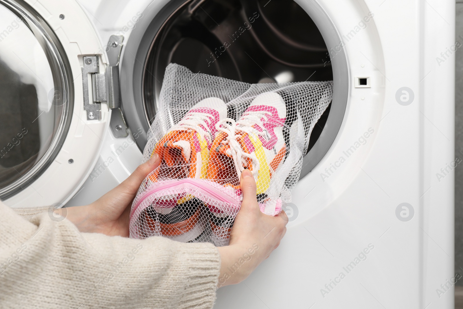 Photo of Woman putting stylish sneakers into washing machine, closeup