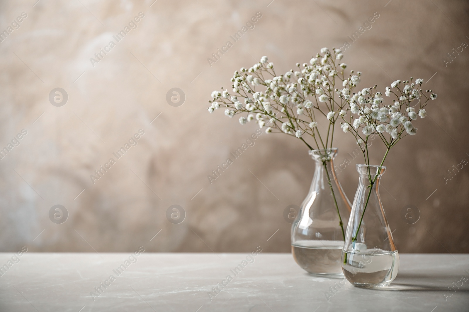 Photo of Gypsophila flowers in vases on table against brown background. Space for text