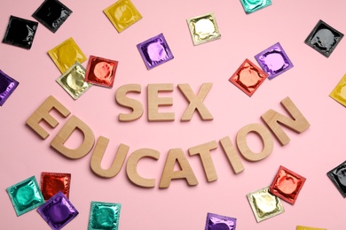 Photo of Flat lay composition with condoms and words SEX EDUCATION made with wooden letters on pink background