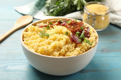 Photo of Tasty millet porridge with bacon, green onion and dill in bowl on light blue wooden table, closeup