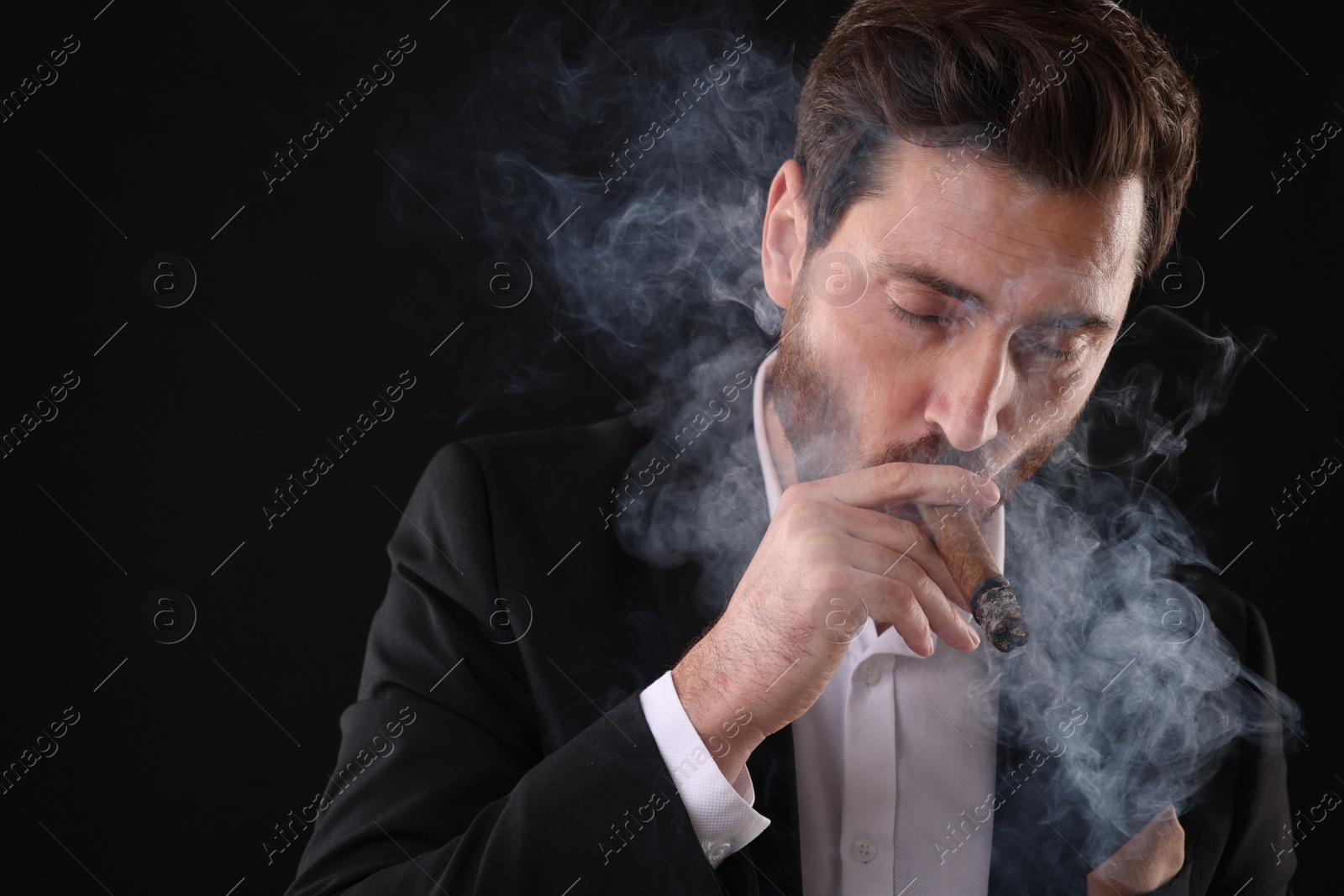 Photo of Handsome man in elegant suit smoking cigar on black background. Space for text