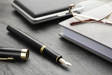 Stylish black fountain pen, glasses, notebook and cigarette case on grey textured table, closeup