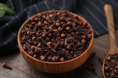 Photo of Bowl and spoon with aromatic cloves on wooden table, closeup