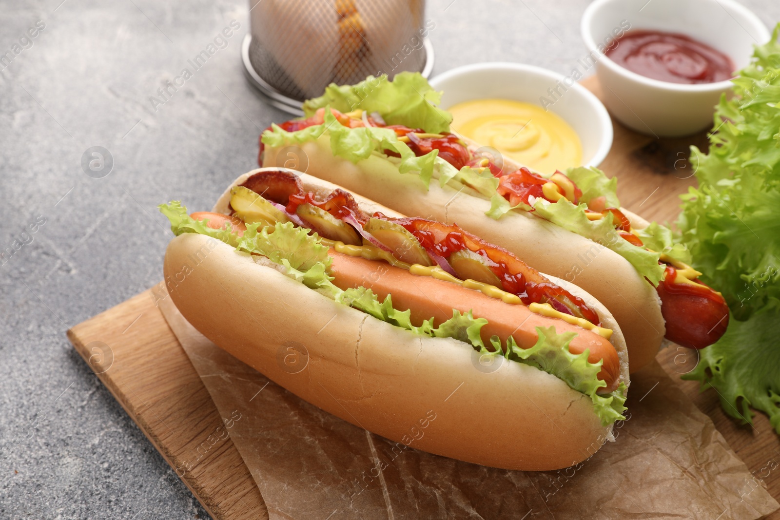 Photo of Delicious hot dogs with lettuce, onion and pickle served on grey table