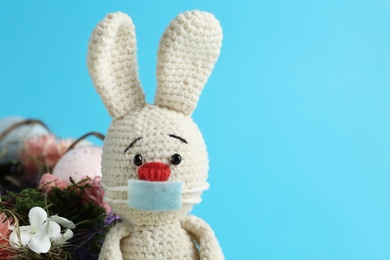Photo of Toy bunny in protective mask on light blue background, space for text. Easter holiday during COVID-19 quarantine