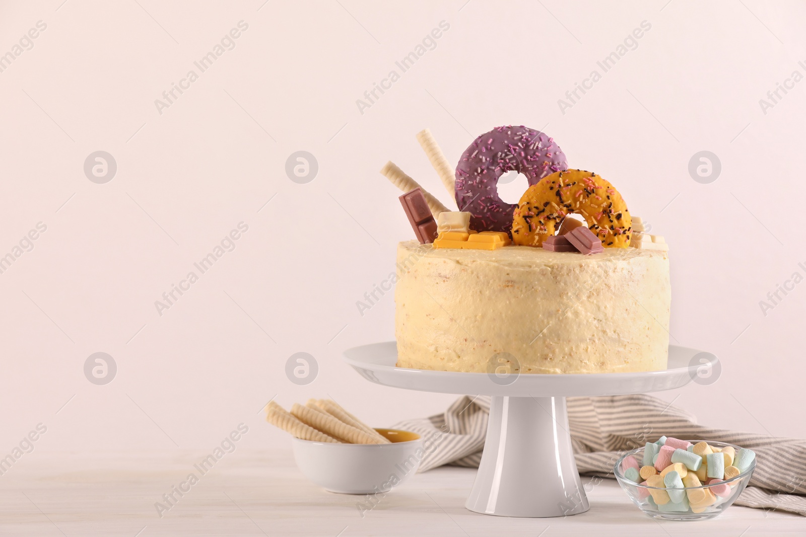 Photo of Delicious cake decorated with sweets, wafer rolls and marshmallows on white wooden table, space for text