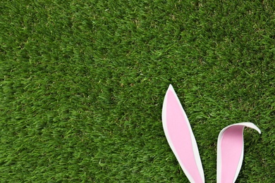 Photo of Funny Easter bunny ears on green grass, top view with space for text