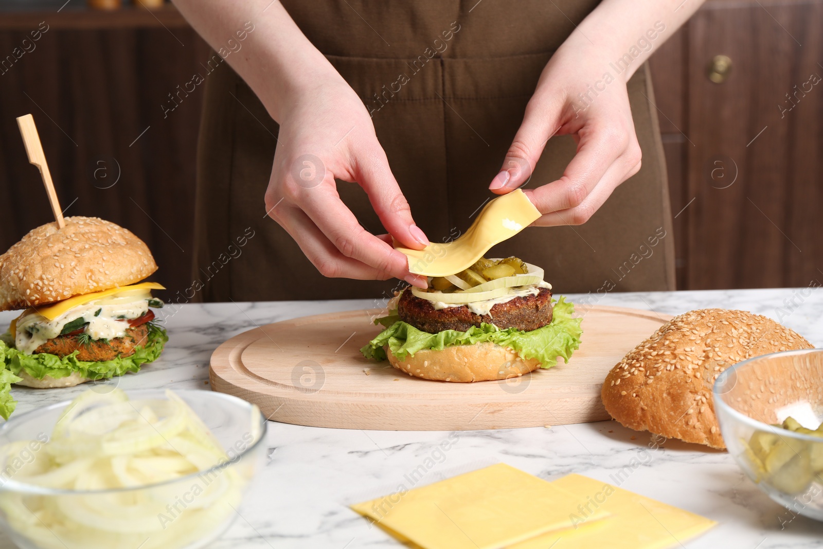 Photo of Woman making delicious vegetarian burger at white marble table, closeup