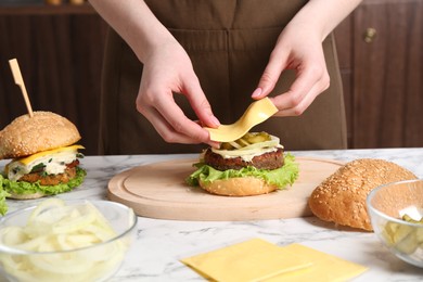 Photo of Woman making delicious vegetarian burger at white marble table, closeup