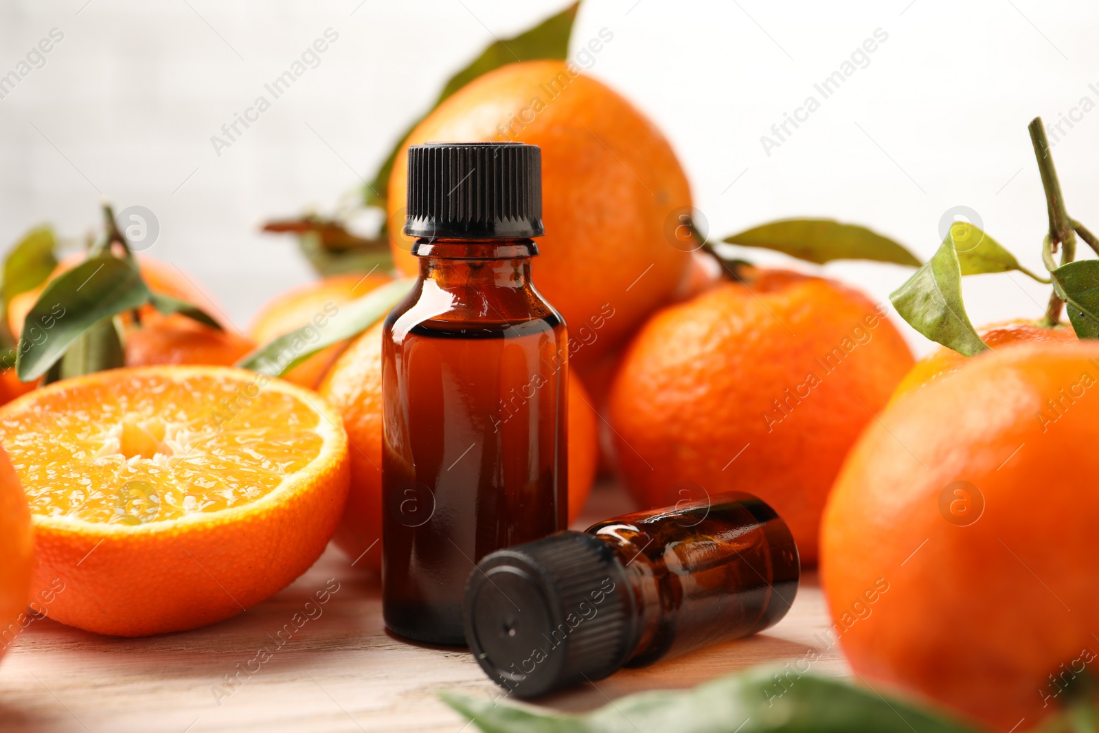 Photo of Bottles of tangerine essential oil and fresh fruits on wooden table, closeup