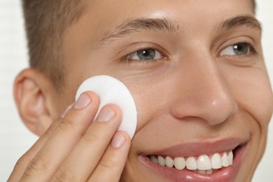 Photo of Handsome man cleaning face with cotton pad, closeup